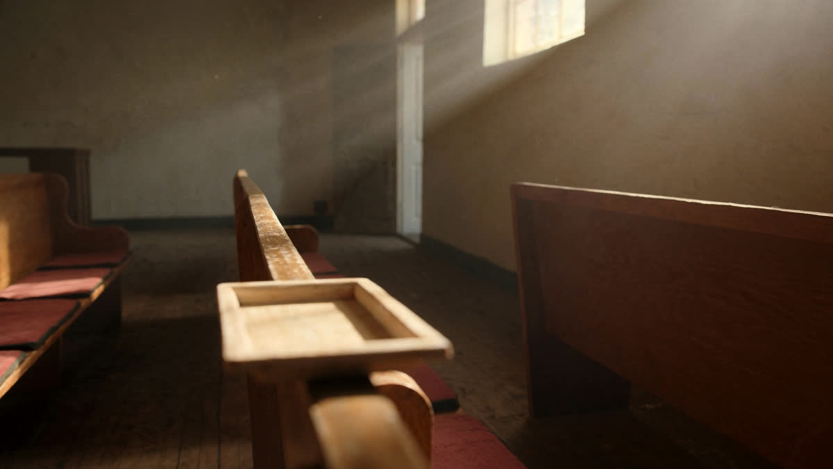 An empty offering plate resting on a wooden church pew in warm morning light