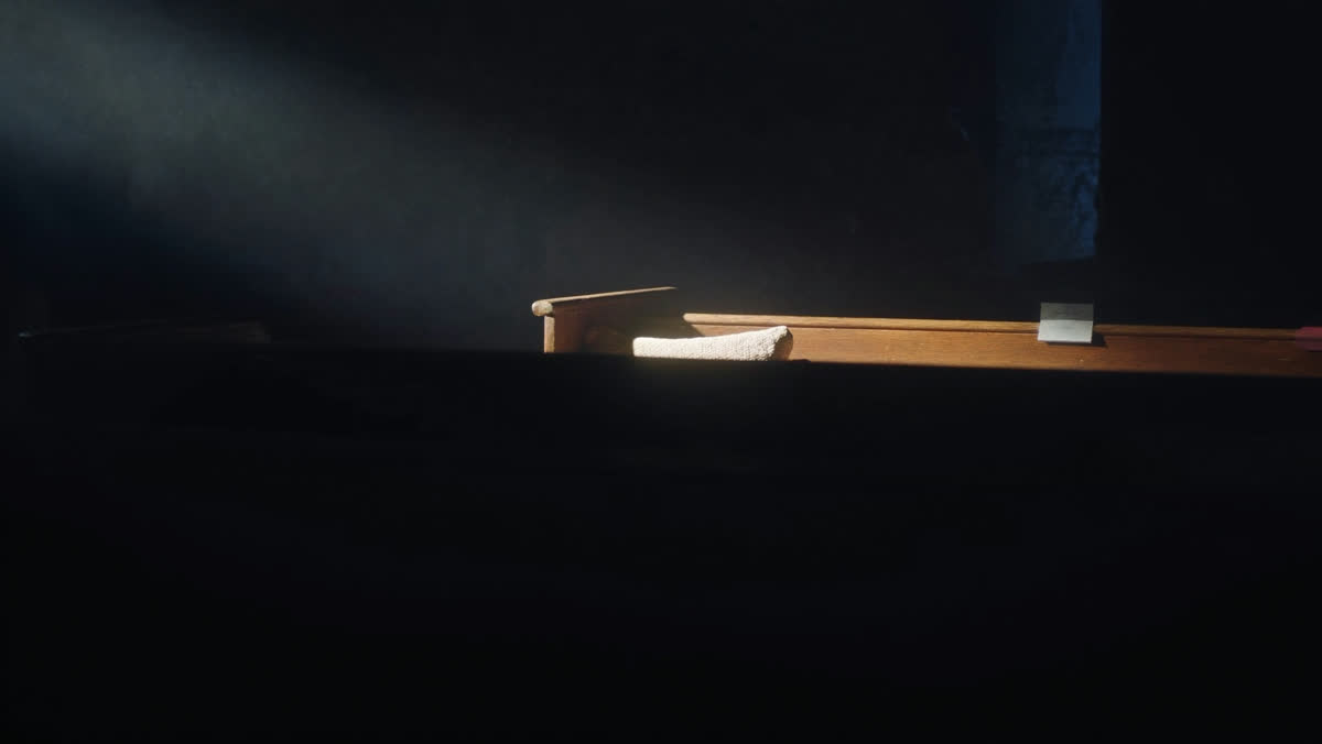 A single empty church pew in shadow with one narrow shaft of light across it