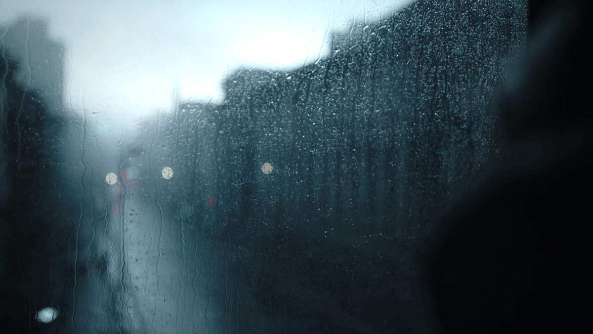 Rain running down a window overlooking a grey city street at dawn