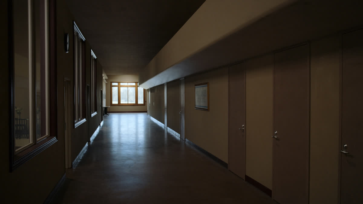 A long empty church corridor lined with closed doors in cool grey daylight