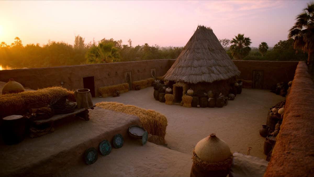 An ancient Egyptian granary courtyard at sunrise with woven baskets of golden wheat, worn stone steps and a clay water j