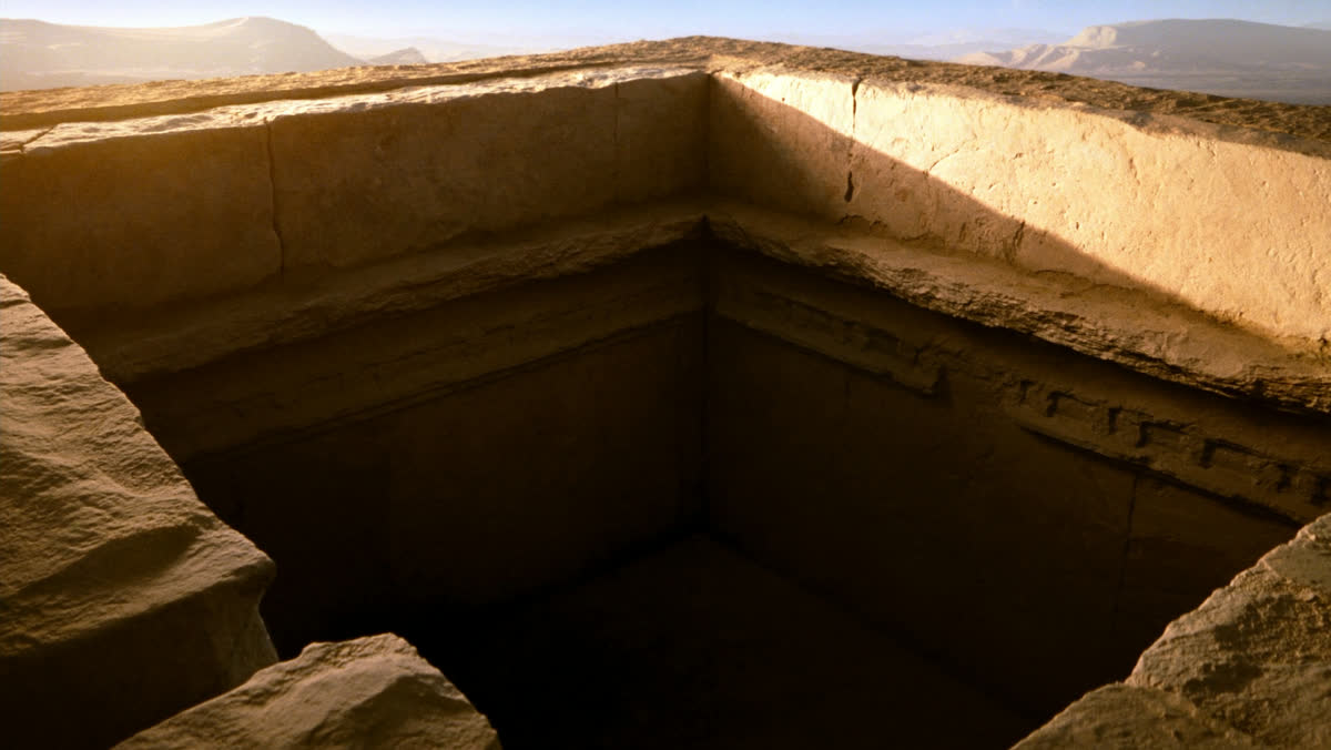 An empty ancient stone cistern in a dry desert landscape at golden hour, rough limestone walls and a shaft of warm sunli